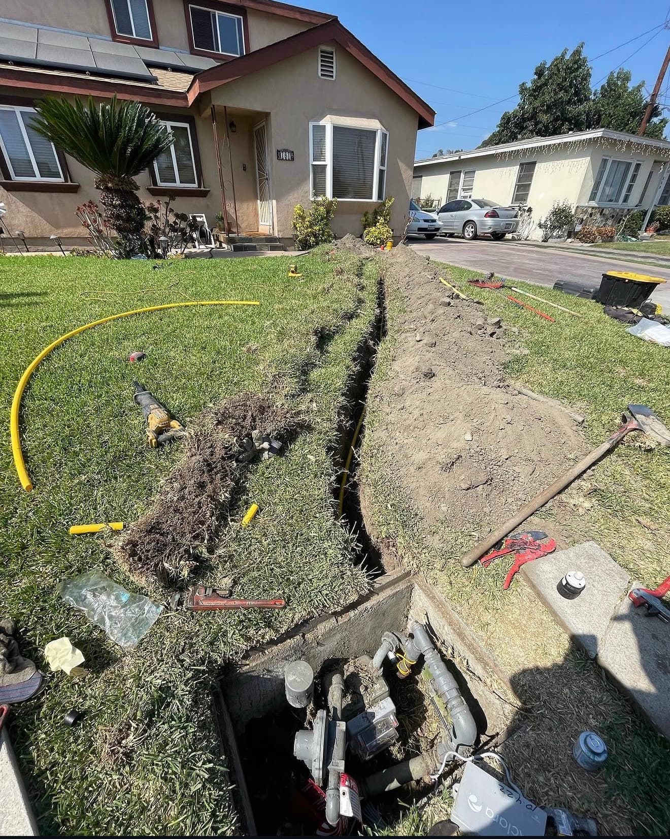 Trench dug through a residential lawn for utility line installation with various tools nearby.