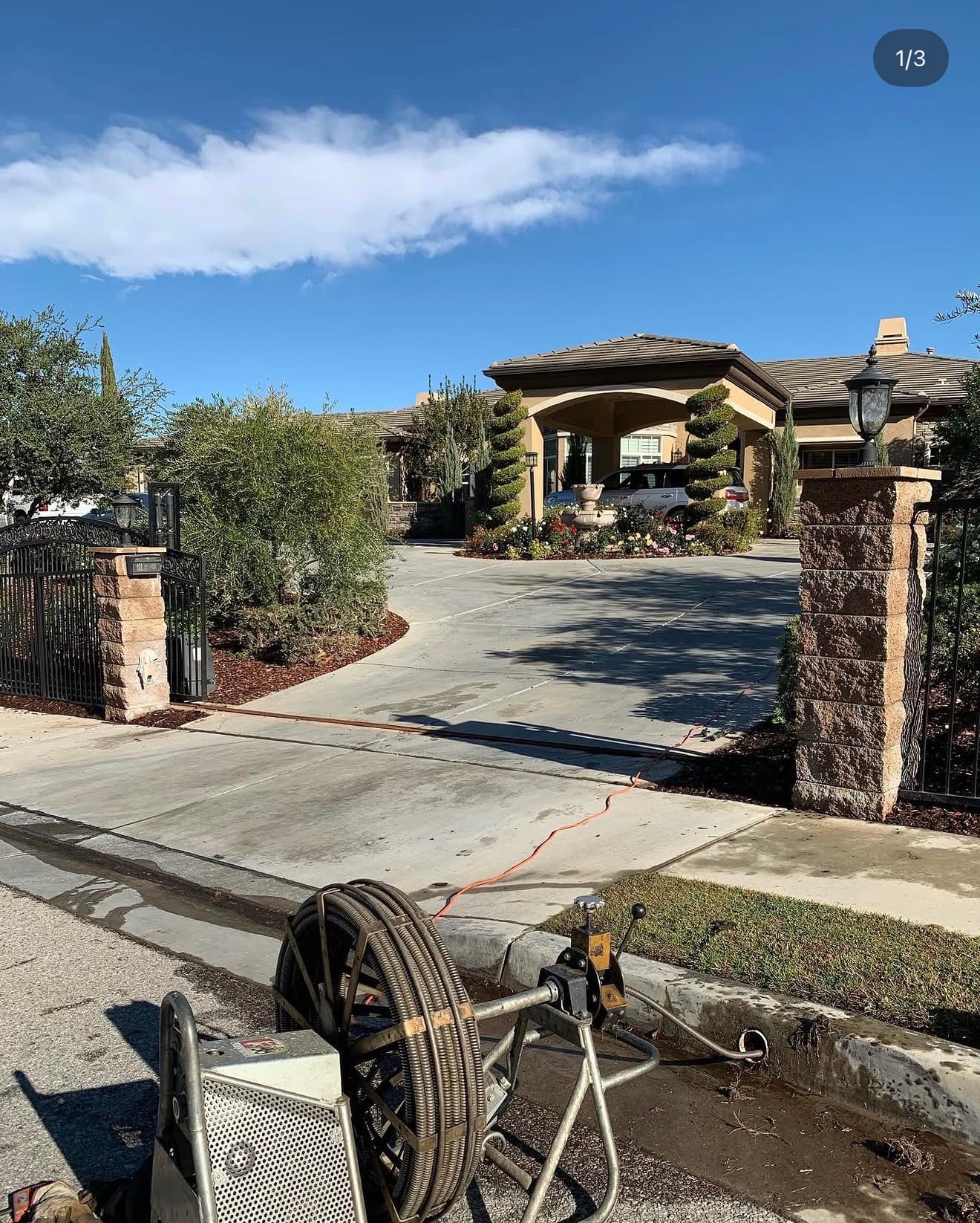 Industrial sewer cleaning equipment on a street outside a large house with a gated driveway.