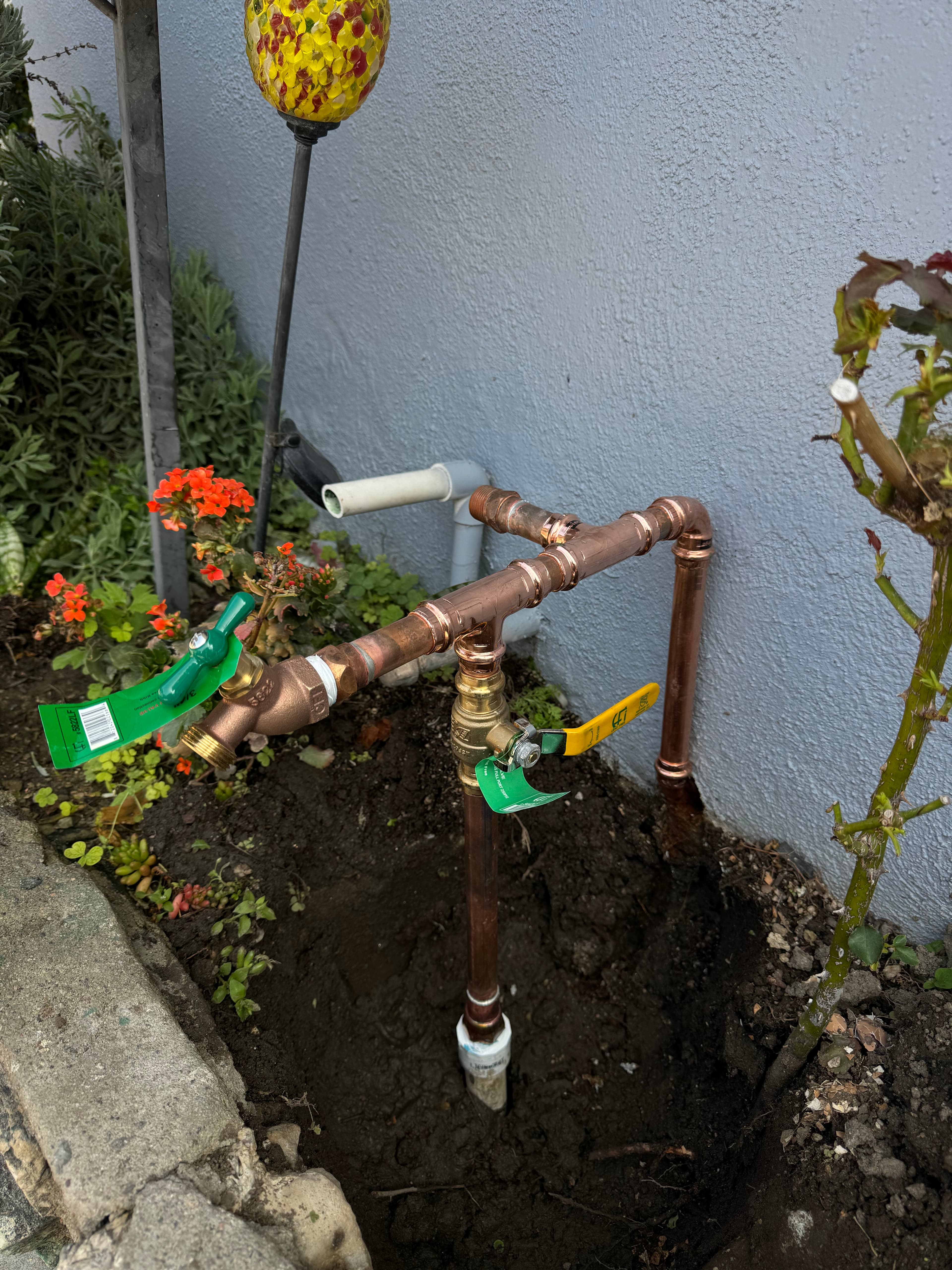 Newly installed copper plumbing with a spigot and yellow ball valve in a garden.